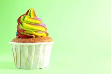 Photo of One delicious cupcake with colorful cream on light green background, closeup. Space for text