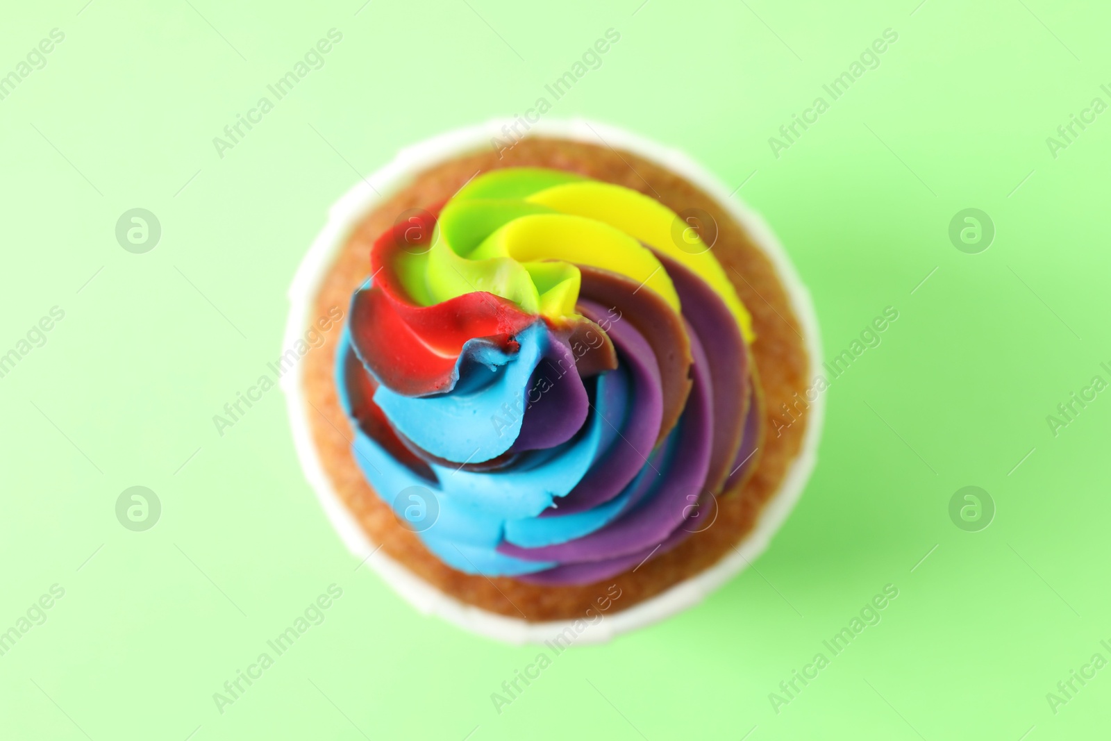 Photo of One delicious cupcake with colorful cream on light green background, top view