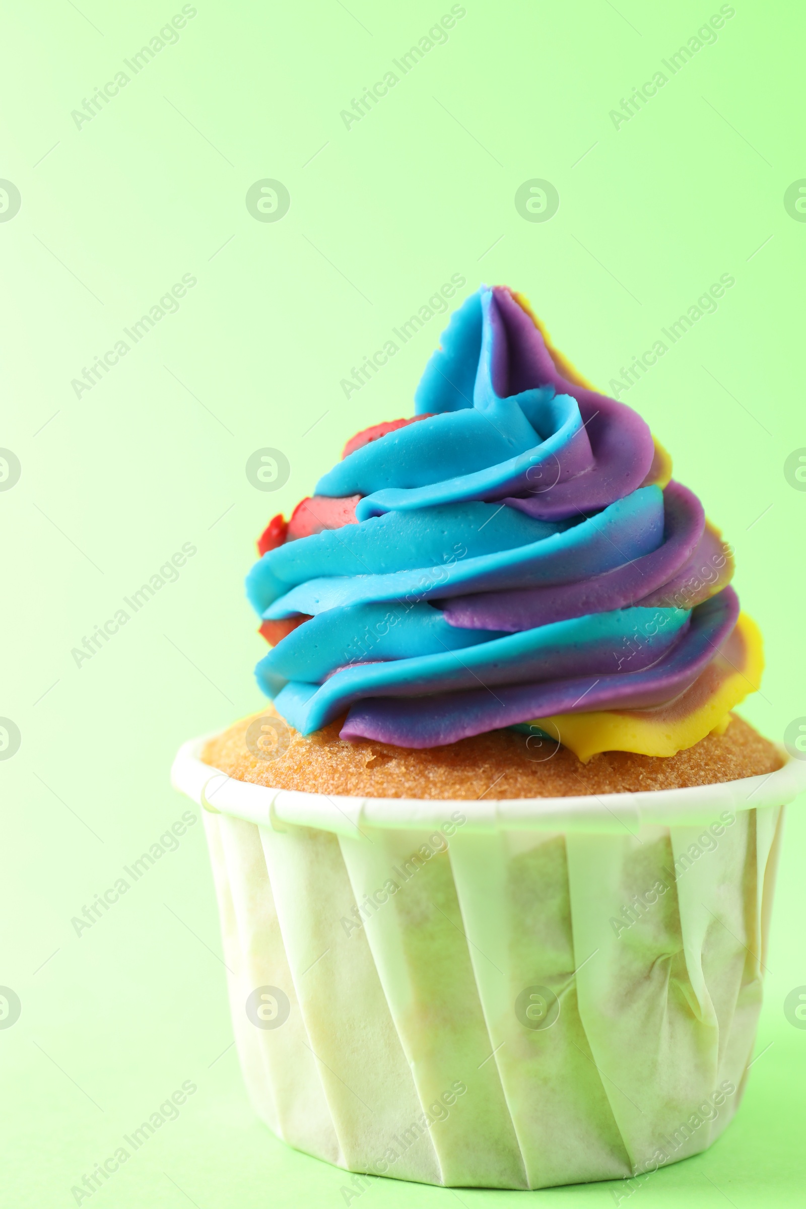 Photo of One delicious cupcake with colorful cream on light green background, closeup