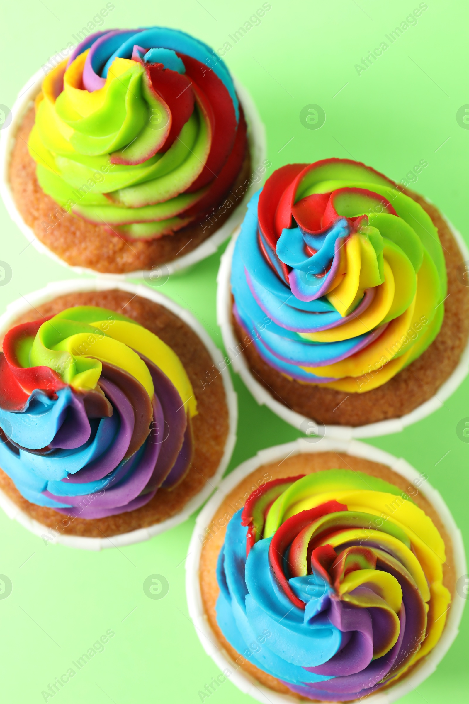 Photo of Delicious cupcakes with colorful cream on light green background, flat lay