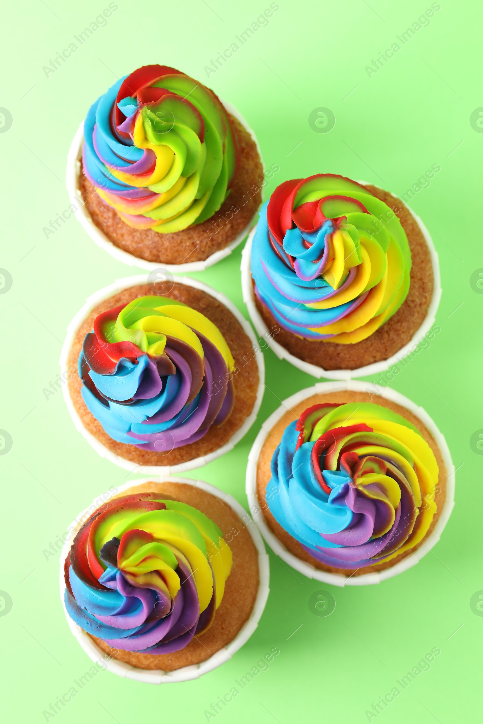 Photo of Delicious cupcakes with colorful cream on light green background, flat lay