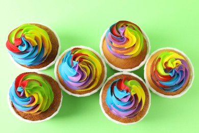 Photo of Delicious cupcakes with colorful cream on light green background, flat lay