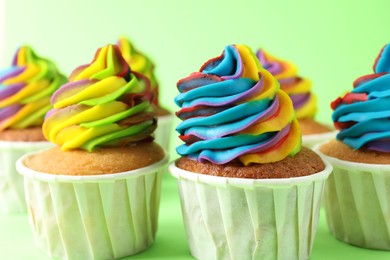 Photo of Delicious cupcakes with colorful cream on light green background, closeup