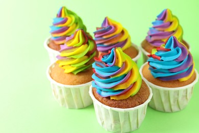 Photo of Delicious cupcakes with colorful cream on light green background, closeup