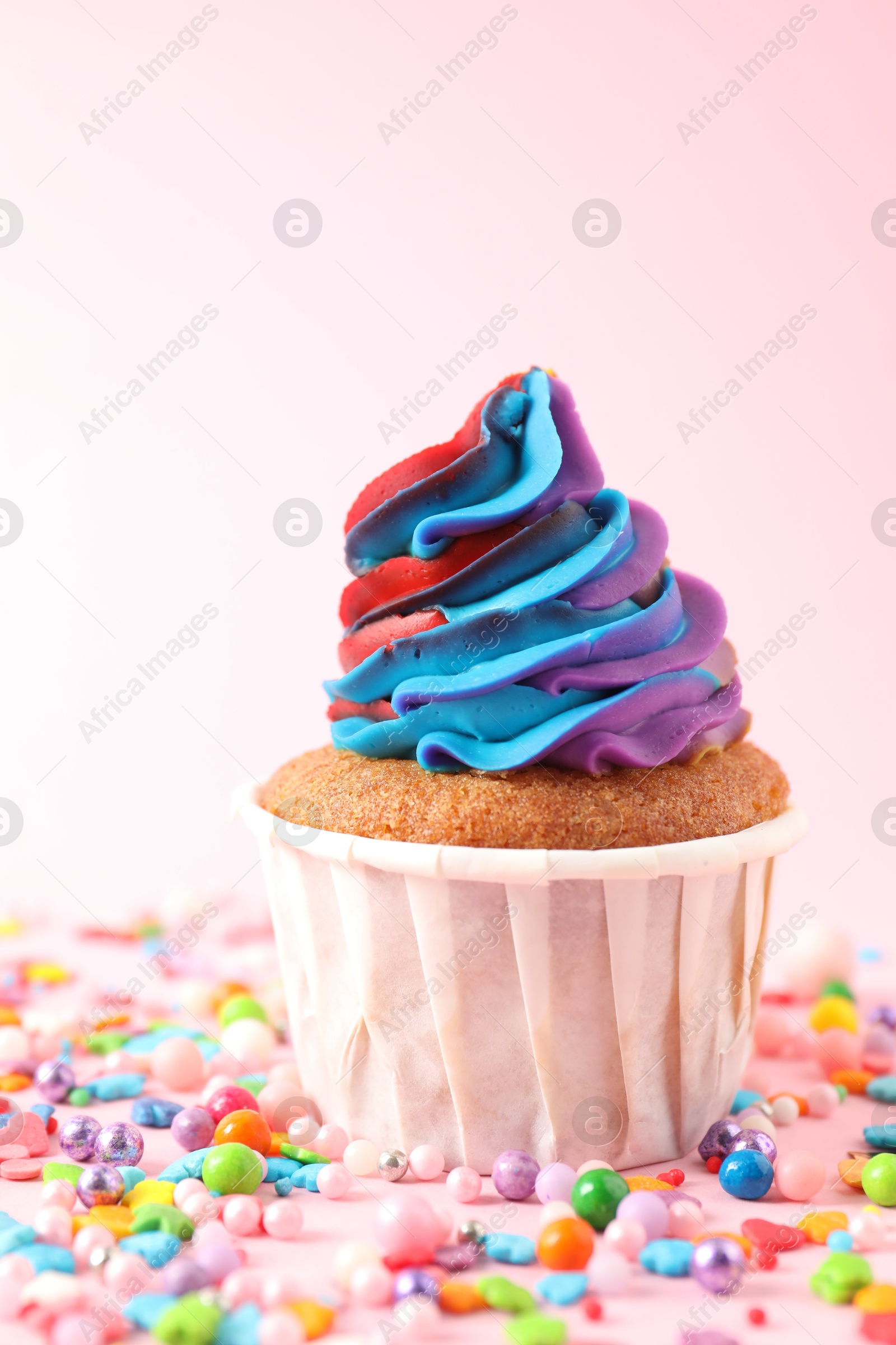 Photo of One delicious cupcake with colorful cream and sprinkles on pink background, closeup