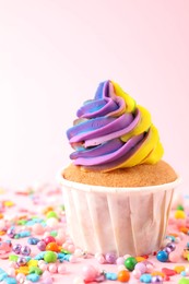 Photo of One delicious cupcake with colorful cream and sprinkles on pink background, closeup