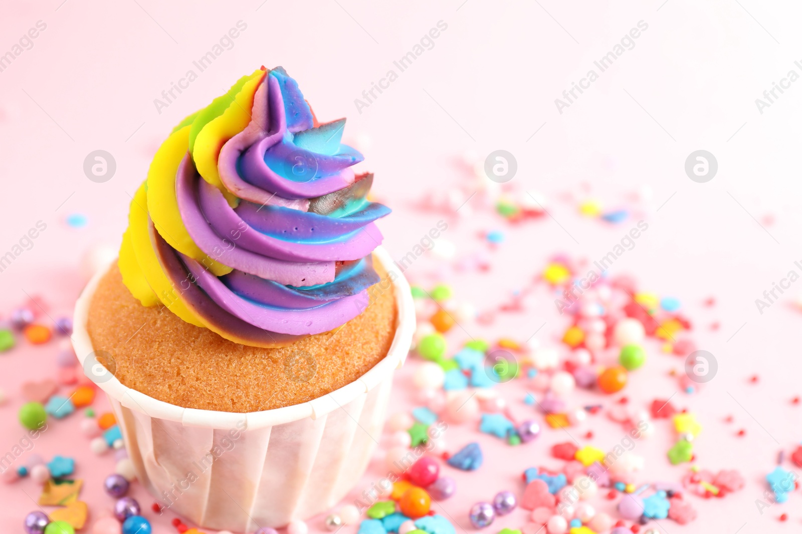 Photo of One delicious cupcake with colorful cream and sprinkles on pink background, closeup. Space for text