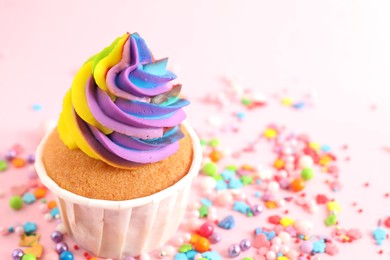 Photo of One delicious cupcake with colorful cream and sprinkles on pink background, closeup. Space for text