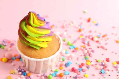 Photo of One delicious cupcake with colorful cream and sprinkles on pink background, closeup. Space for text