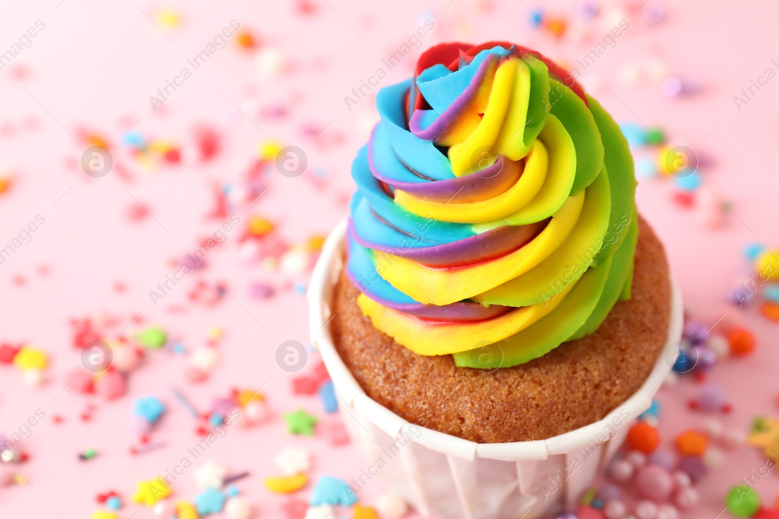 Photo of One delicious cupcake with colorful cream and sprinkles on pink background, closeup. Space for text