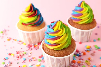 Photo of Delicious cupcakes with colorful cream and sprinkles on pink background, closeup