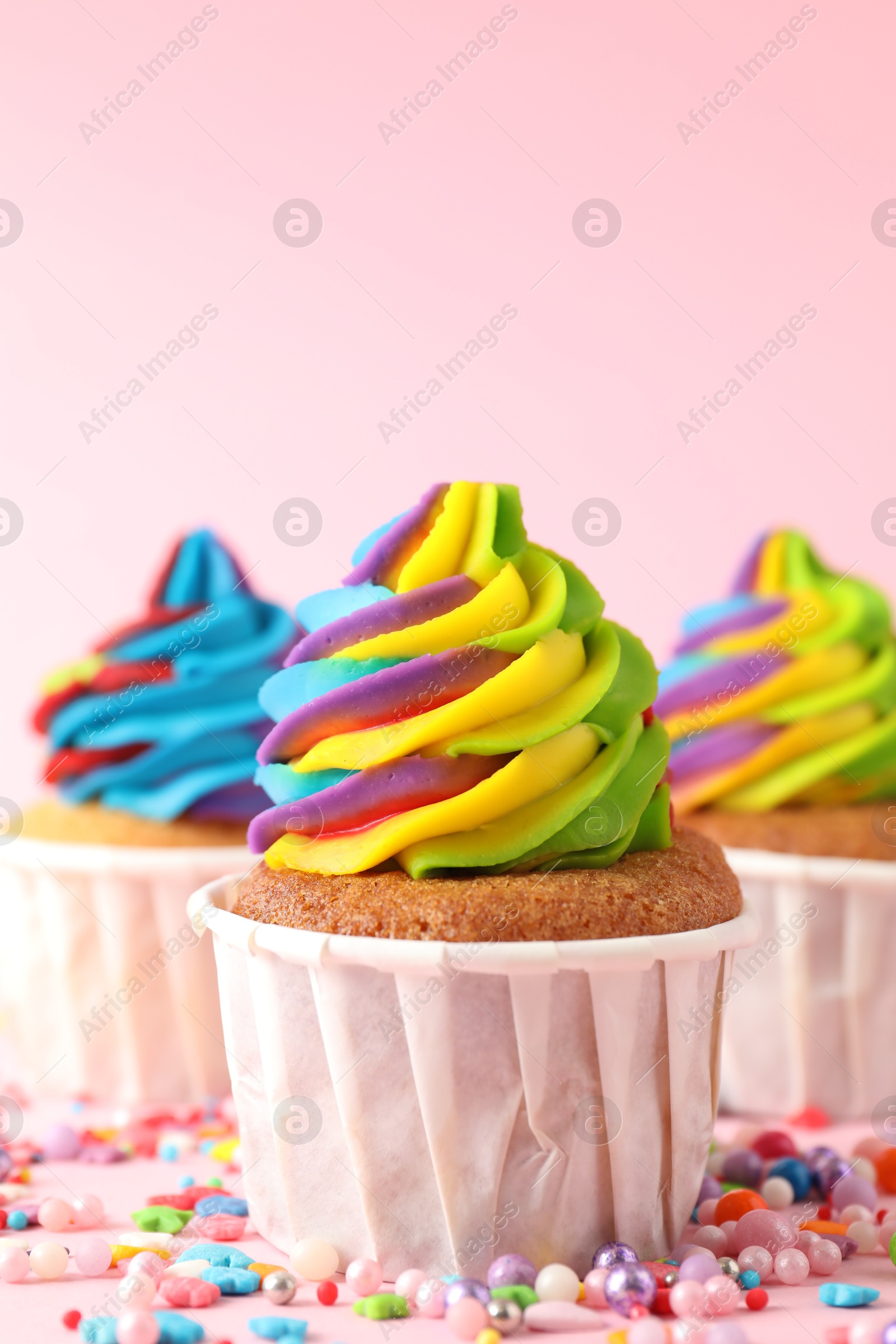 Photo of Delicious cupcakes with colorful cream and sprinkles on pink background, closeup