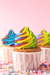 Photo of Delicious cupcakes with colorful cream and sprinkles on pink background, closeup