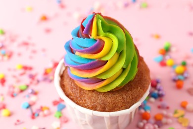 Photo of One delicious cupcake with colorful cream and sprinkles on pink background, closeup