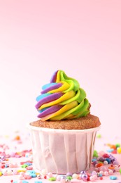 Photo of One delicious cupcake with colorful cream and sprinkles on pink background, closeup