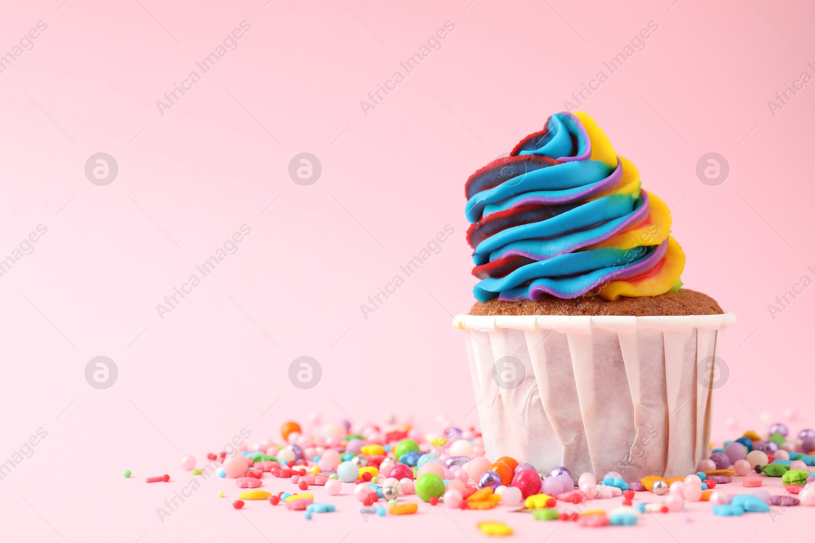 Photo of One delicious cupcake with colorful cream and sprinkles on pink background, closeup. Space for text