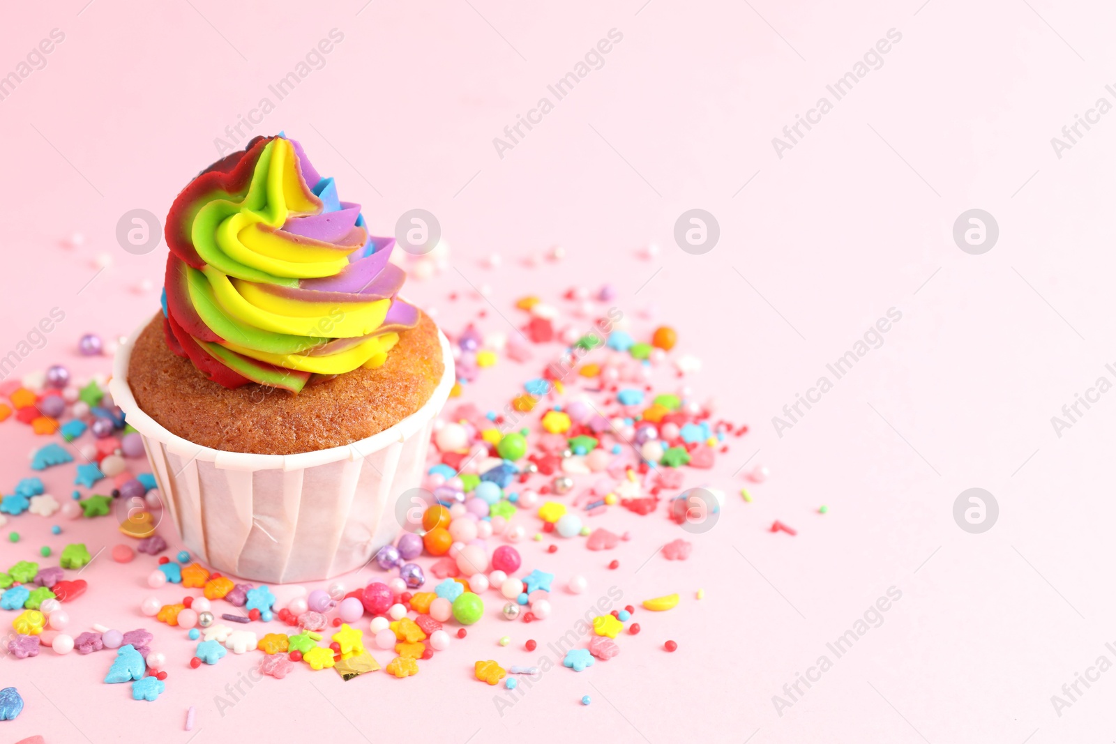 Photo of One delicious cupcake with colorful cream and sprinkles on pink background, closeup. Space for text