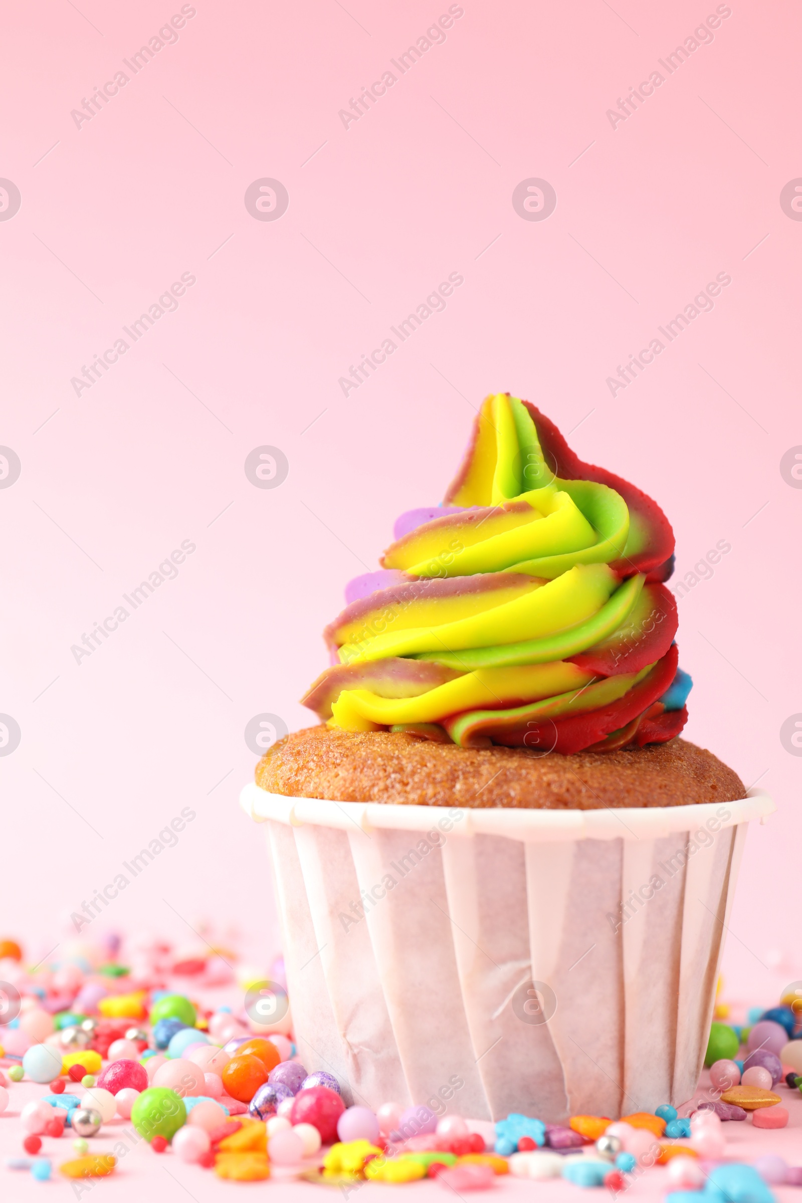 Photo of One delicious cupcake with colorful cream and sprinkles on pink background, closeup