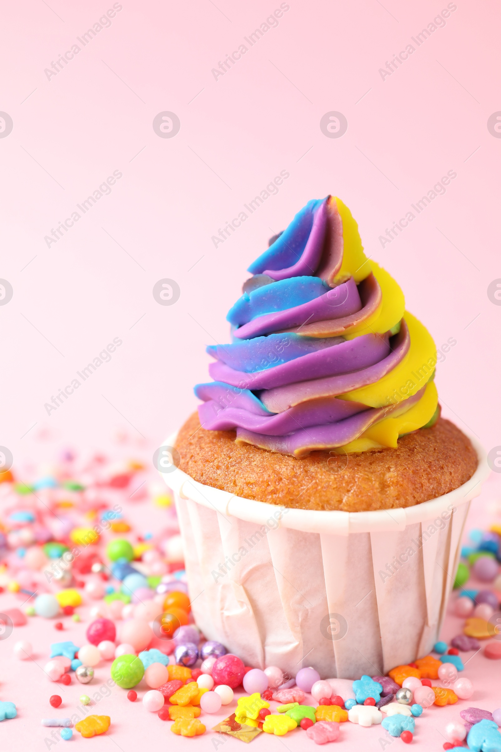 Photo of One delicious cupcake with colorful cream and sprinkles on pink background, closeup