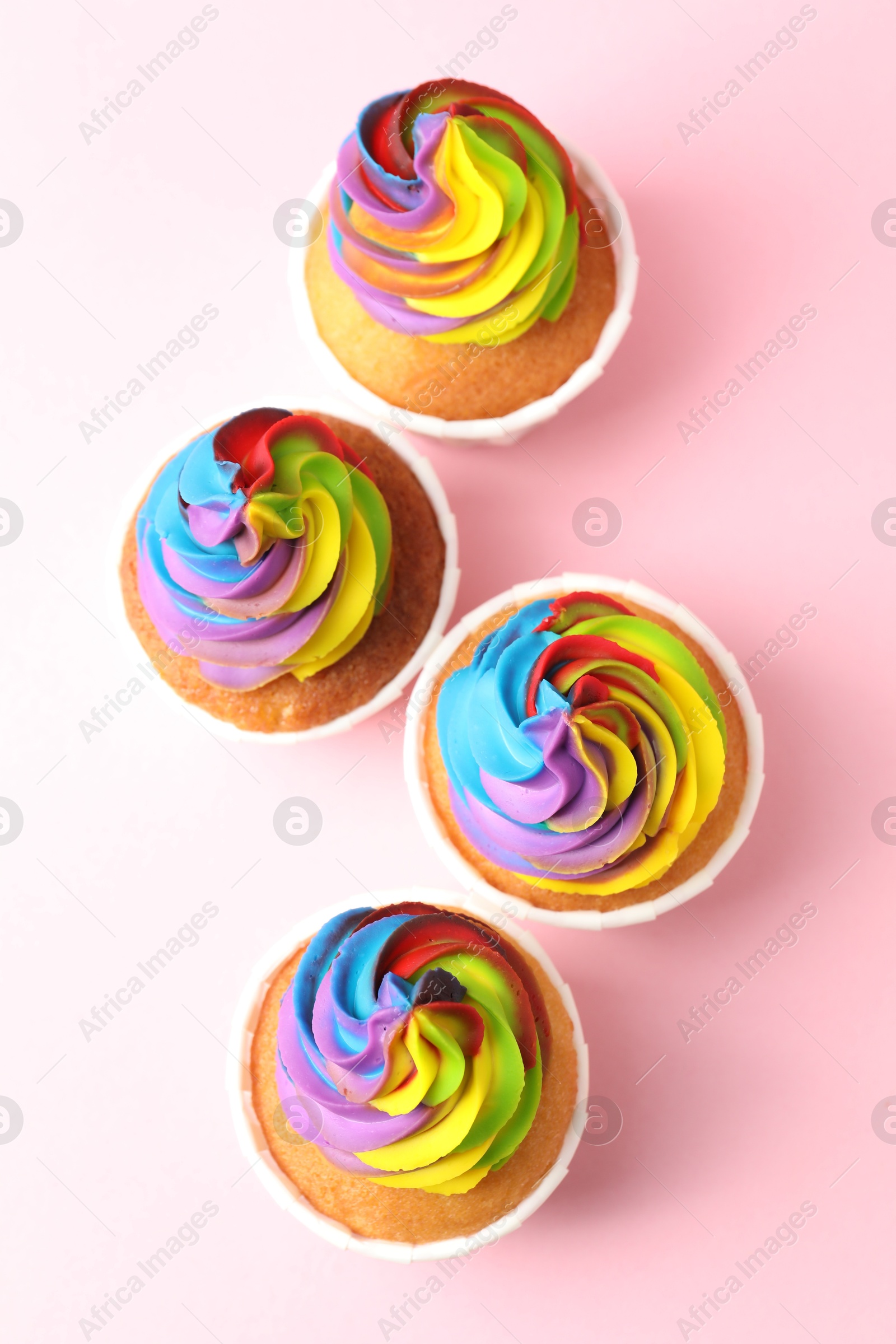 Photo of Delicious cupcakes with colorful cream on pink background, flat lay