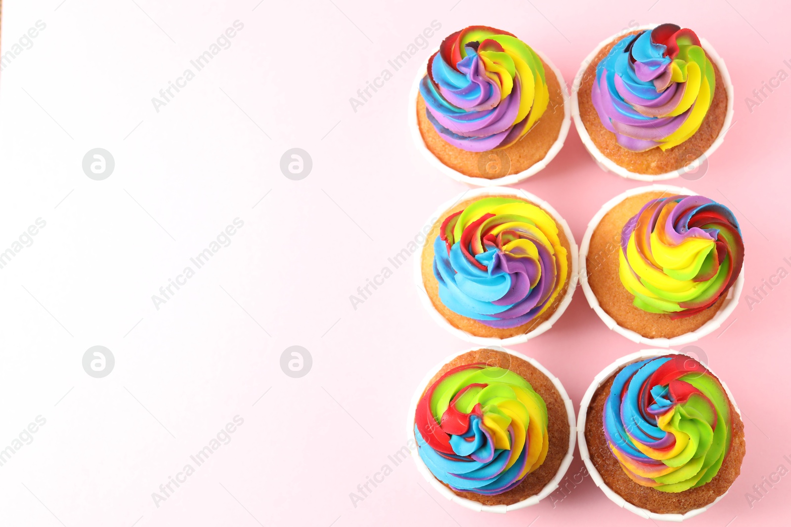 Photo of Delicious cupcakes with colorful cream on pink background, flat lay. Space for text