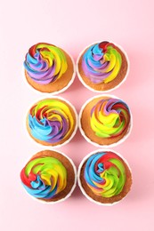 Photo of Delicious cupcakes with colorful cream on pink background, flat lay