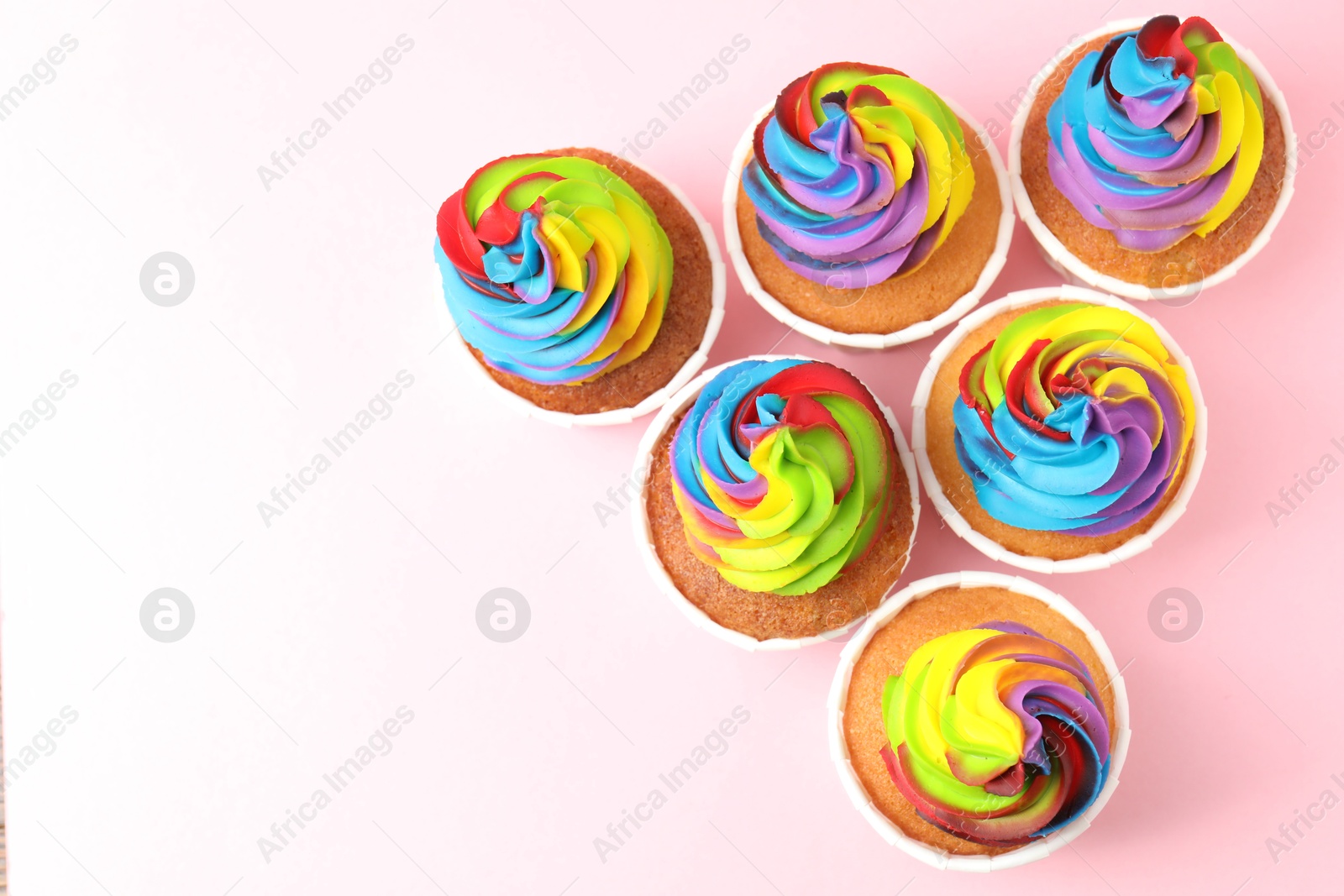 Photo of Delicious cupcakes with colorful cream on pink background, flat lay. Space for text