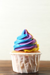 Photo of Delicious cupcake with colorful cream on wooden table against white background, closeup