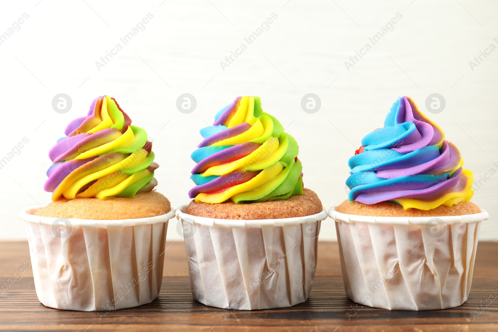 Photo of Delicious cupcakes with colorful cream on wooden table against white background, closeup