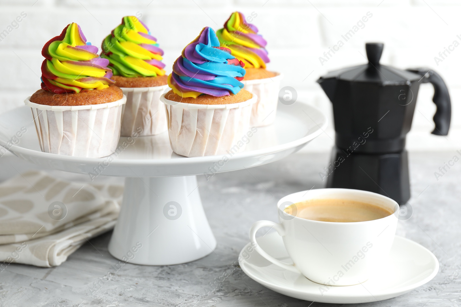 Photo of Delicious cupcakes with colorful cream and cup of coffee on grey textured table, closeup