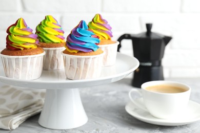 Photo of Delicious cupcakes with colorful cream and cup of coffee on grey textured table, closeup