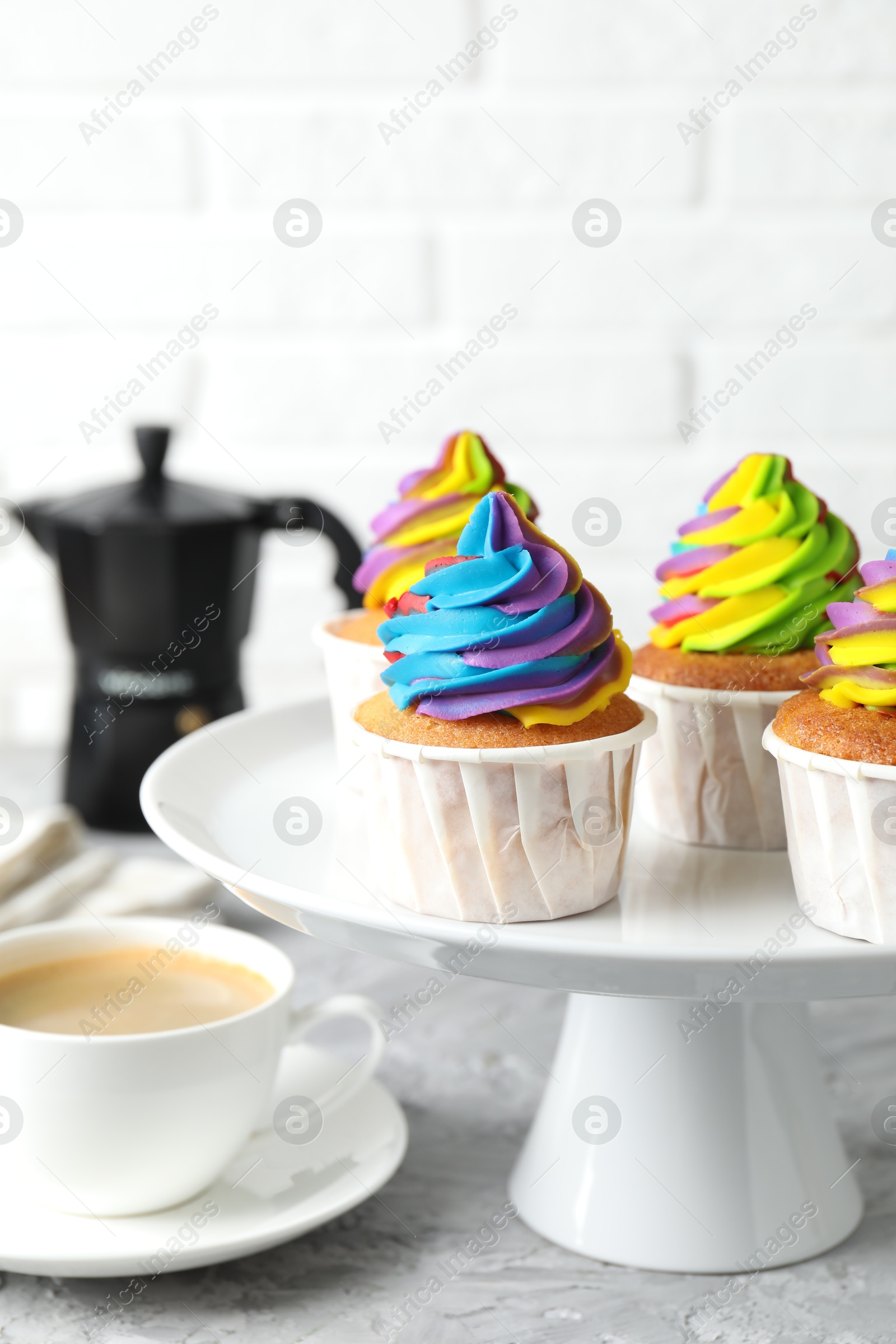 Photo of Delicious cupcakes with colorful cream and cup of coffee on grey textured table, closeup