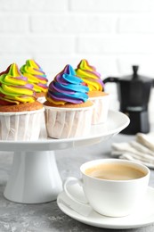 Photo of Delicious cupcakes with colorful cream and cup of coffee on grey textured table, closeup