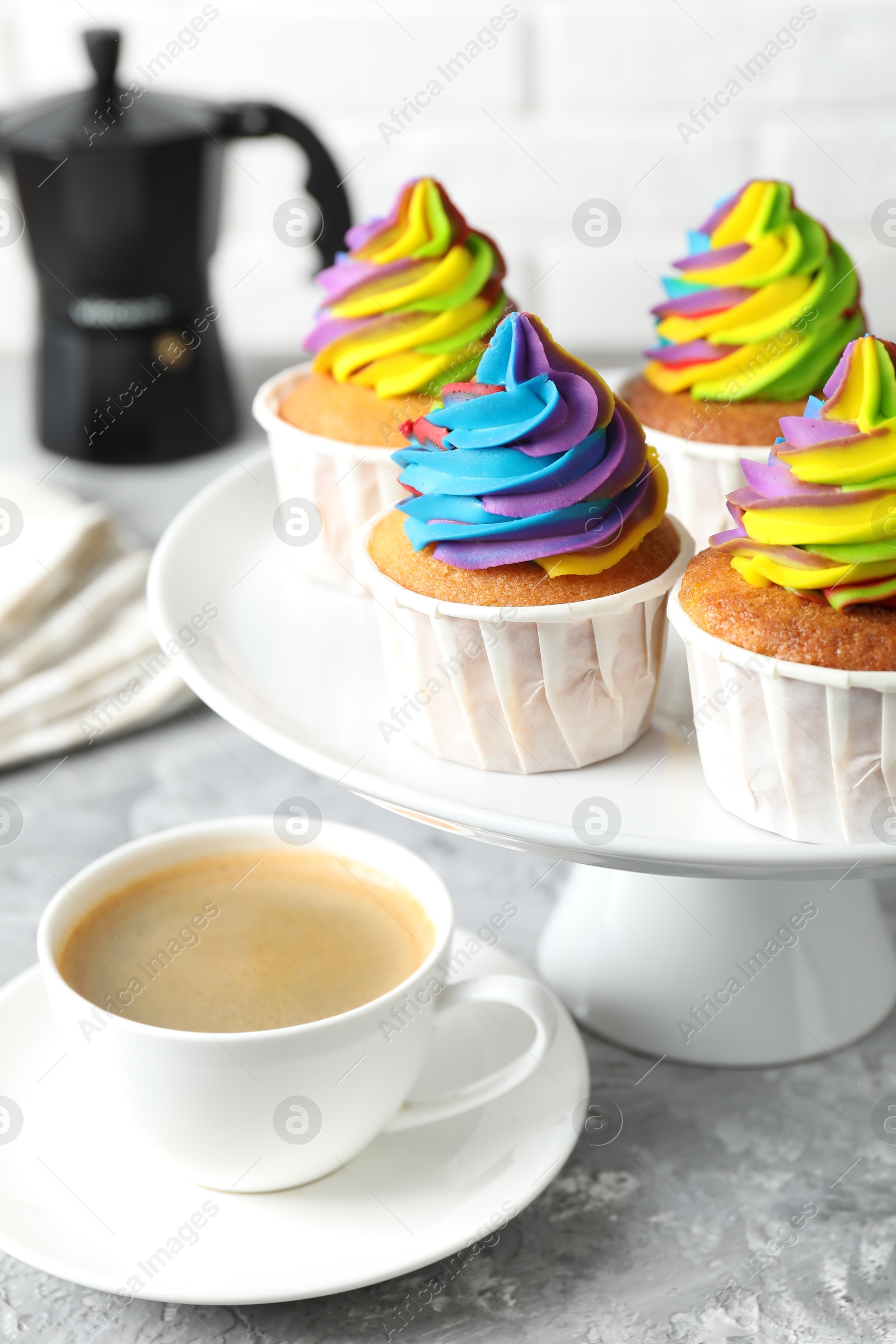 Photo of Delicious cupcakes with colorful cream and cup of coffee on grey textured table, closeup