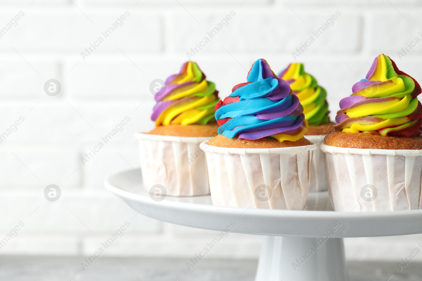 Photo of Delicious cupcakes with colorful cream on stand against blurred white background, closeup. Space for text