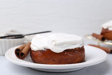 Photo of Tasty cinnamon roll with cream and spices on light table, closeup