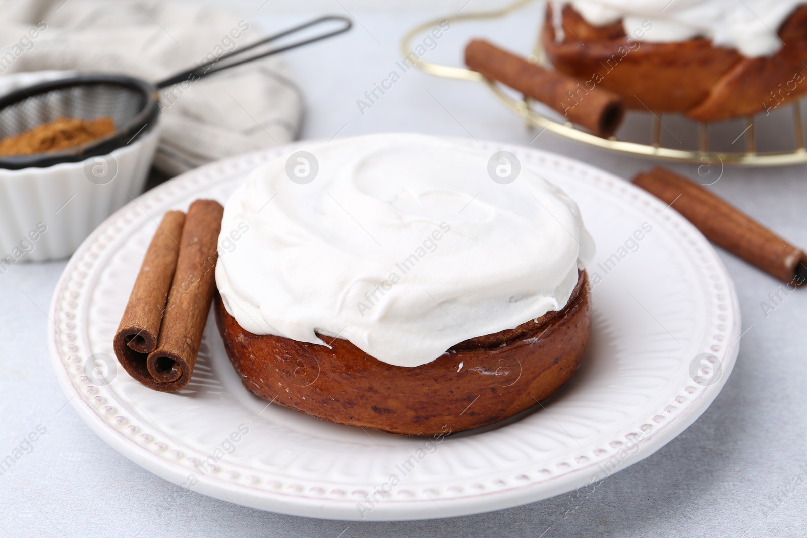 Photo of Tasty cinnamon roll with cream and spices on light table, closeup