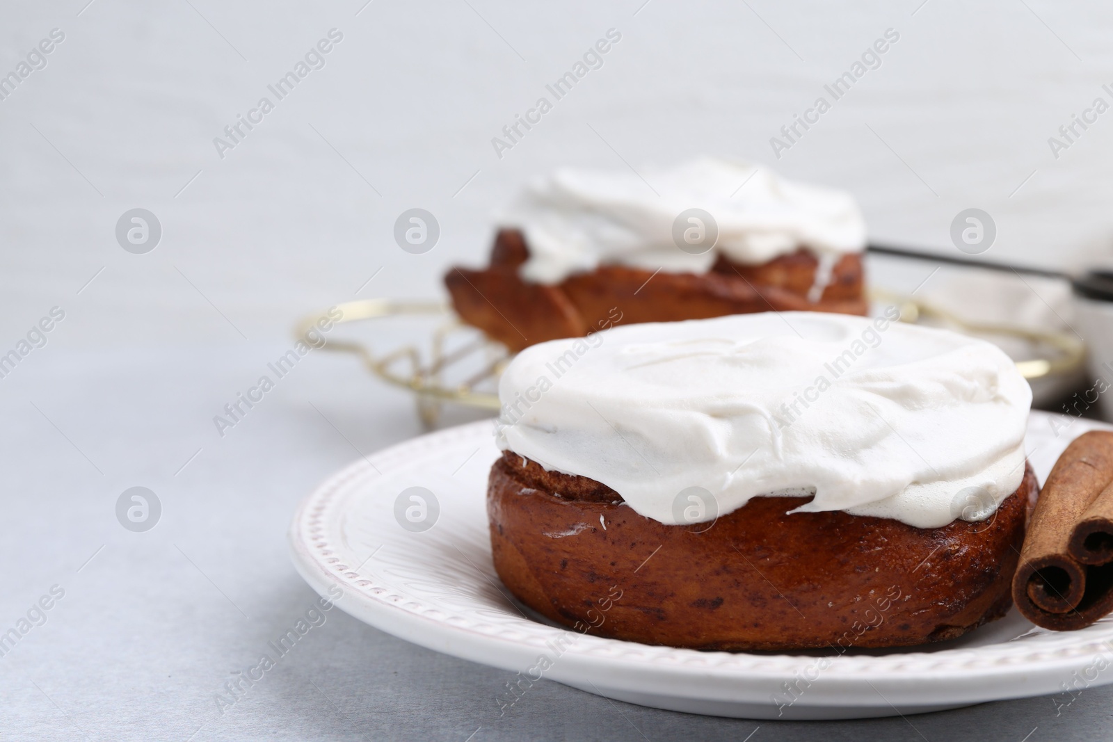 Photo of Tasty cinnamon rolls with cream and stick on light table, closeup. Space for text