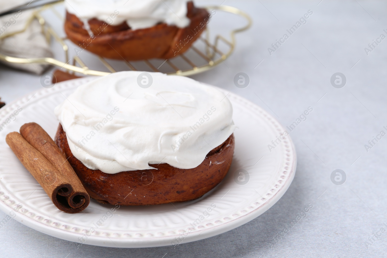 Photo of Tasty cinnamon rolls with cream and stick on light table, closeup