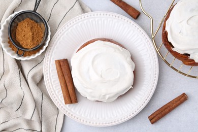 Photo of Tasty cinnamon rolls with cream and spices on light table, flat lay