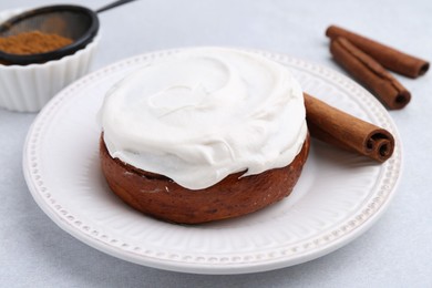 Photo of Tasty cinnamon roll with cream and spices on light table, closeup