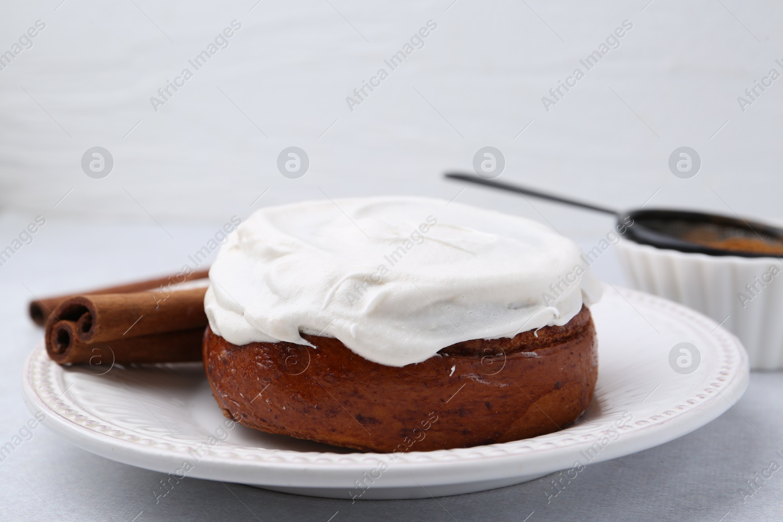 Photo of Tasty cinnamon roll with cream and spices on light table, closeup