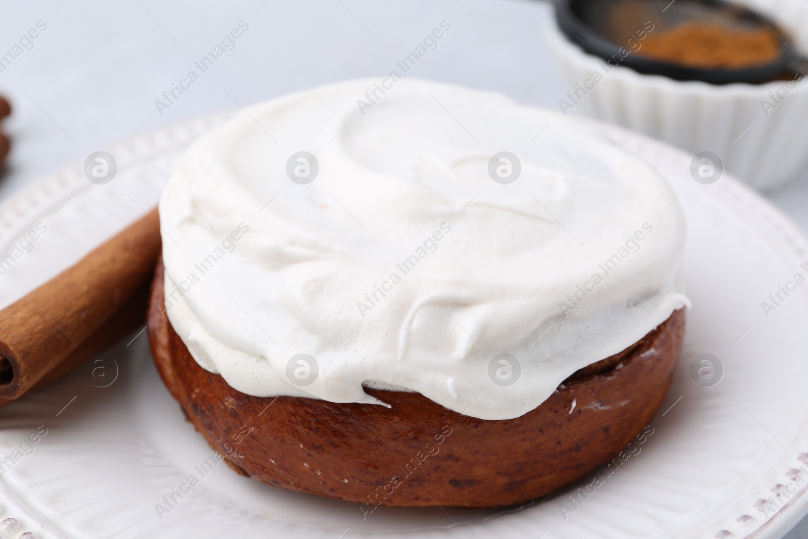 Photo of Tasty cinnamon roll with cream and stick on table, closeup