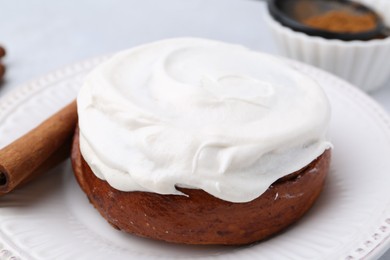 Photo of Tasty cinnamon roll with cream and stick on table, closeup