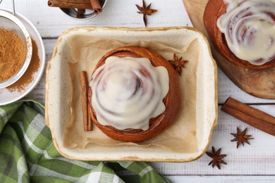 Photo of Tasty cinnamon rolls with cream and spices on white wooden table, flat lay