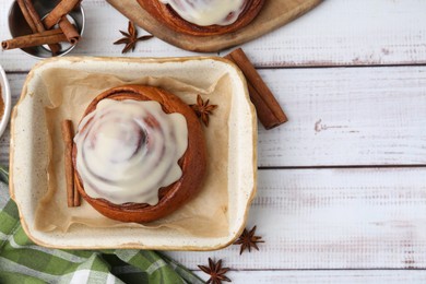 Photo of Tasty cinnamon rolls with cream and spices on white wooden table, flat lay. Space for text