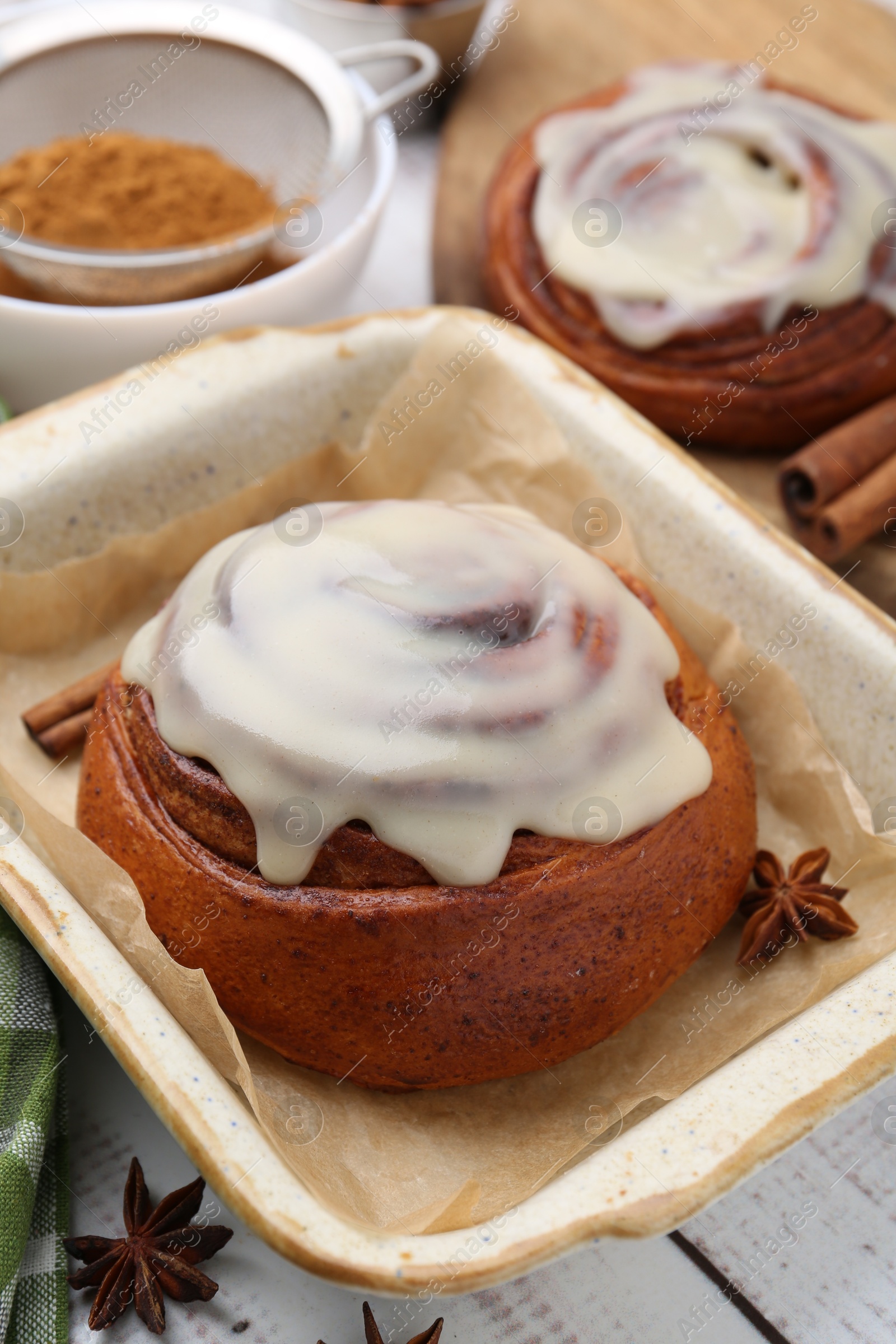 Photo of Tasty cinnamon rolls with cream and spices on white wooden table, closeup