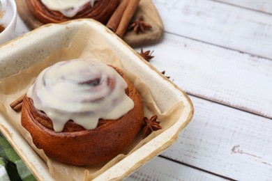 Photo of Tasty cinnamon roll with cream and spices on white wooden table, closeup. Space for text