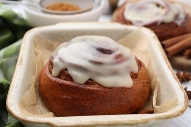 Photo of Tasty cinnamon roll with cream in baking dish and spices on table, closeup