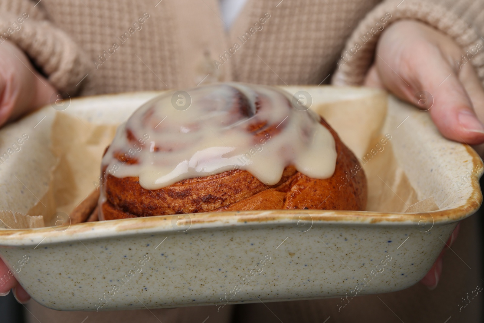 Photo of Woman holding baking dish with tasty cinnamon roll, closeup